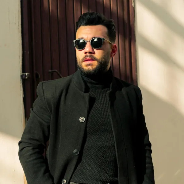 A confident professional man wearing a premium black turtleneck and wool coat, showcasing perfect hair system image continuity and the NSY Duo-System standard.